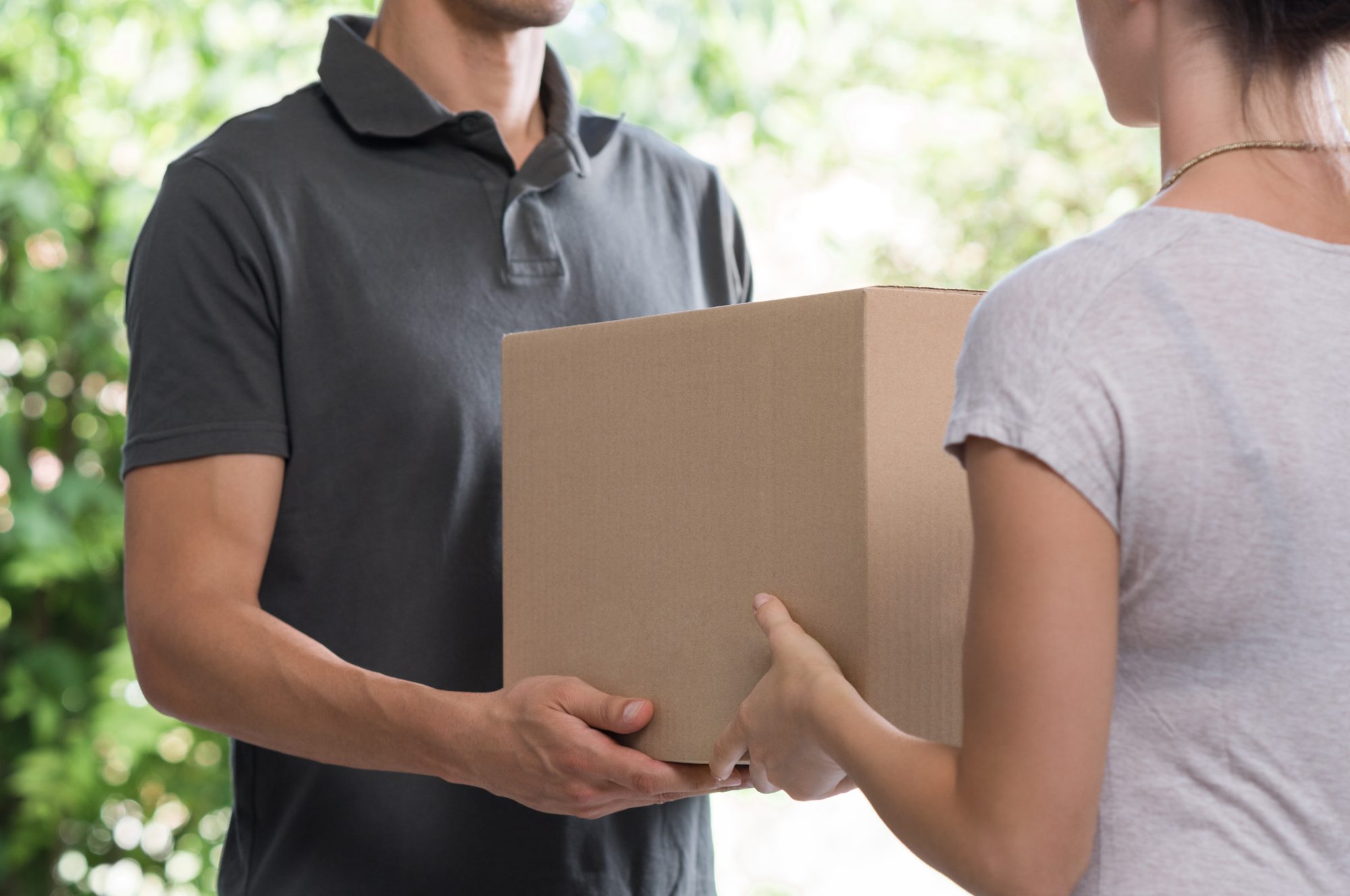 Woman and courier during order transfer. Woman accepting delivery from deliveryman. Cropped image of delivery service worker giving parcel to client.